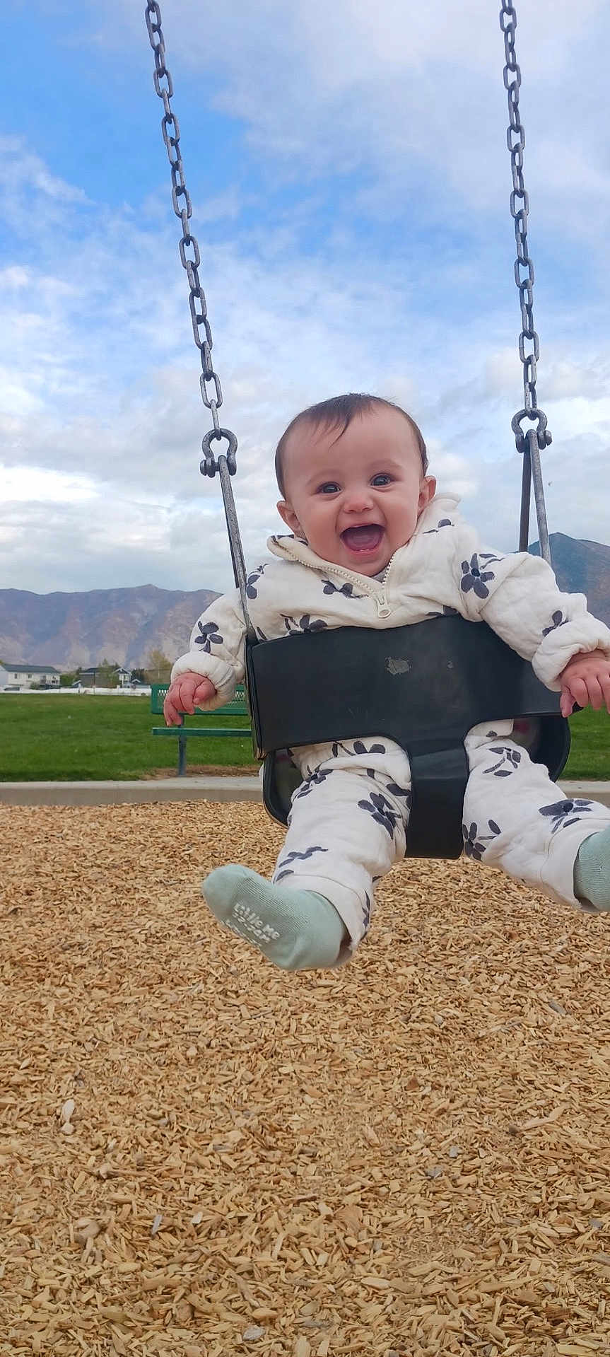 Aayla joined the competition — help win amazing prizes! baby, child, swing, playground, outdoor, smiling, happy, clothing, jacket, mountains, sky, clouds, woodchips, seat, chains, bench, grass, person, feet, sock