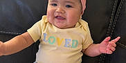 Aizlynn joined the competition — help win amazing prizes! baby, child, smile, headband, pink_bow, shirt, yellow_shirt, text_on_clothing, couch, blanket, indoor, happy, cute, person, infant, seated, furniture, soft_texture, chubby_cheeks, casual_clothing
