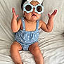 baby, child, sunglasses, headband, bow, blue_outfit, sitting, blanket, indoors, cute, expression, hands_up, feet, soft_texture, portrait, fashion, infant, comfortable, white_background, playful