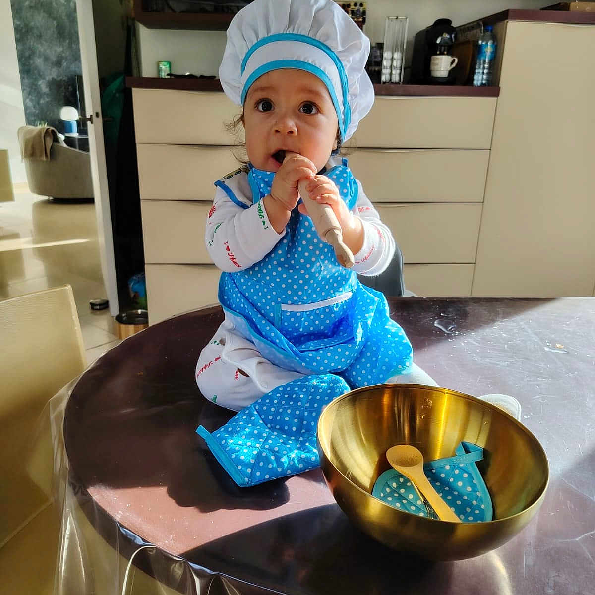Faridou a rejoint le concours — aidez-le/la à gagner de superbes lots ! appliance, baby, blue_apron, bowl, cabinet, chef_hat, child, cooking, cute, indoor, kitchen, light, person, playful, pot_holder, shadow, smiling, table, toddler, wooden_spoon