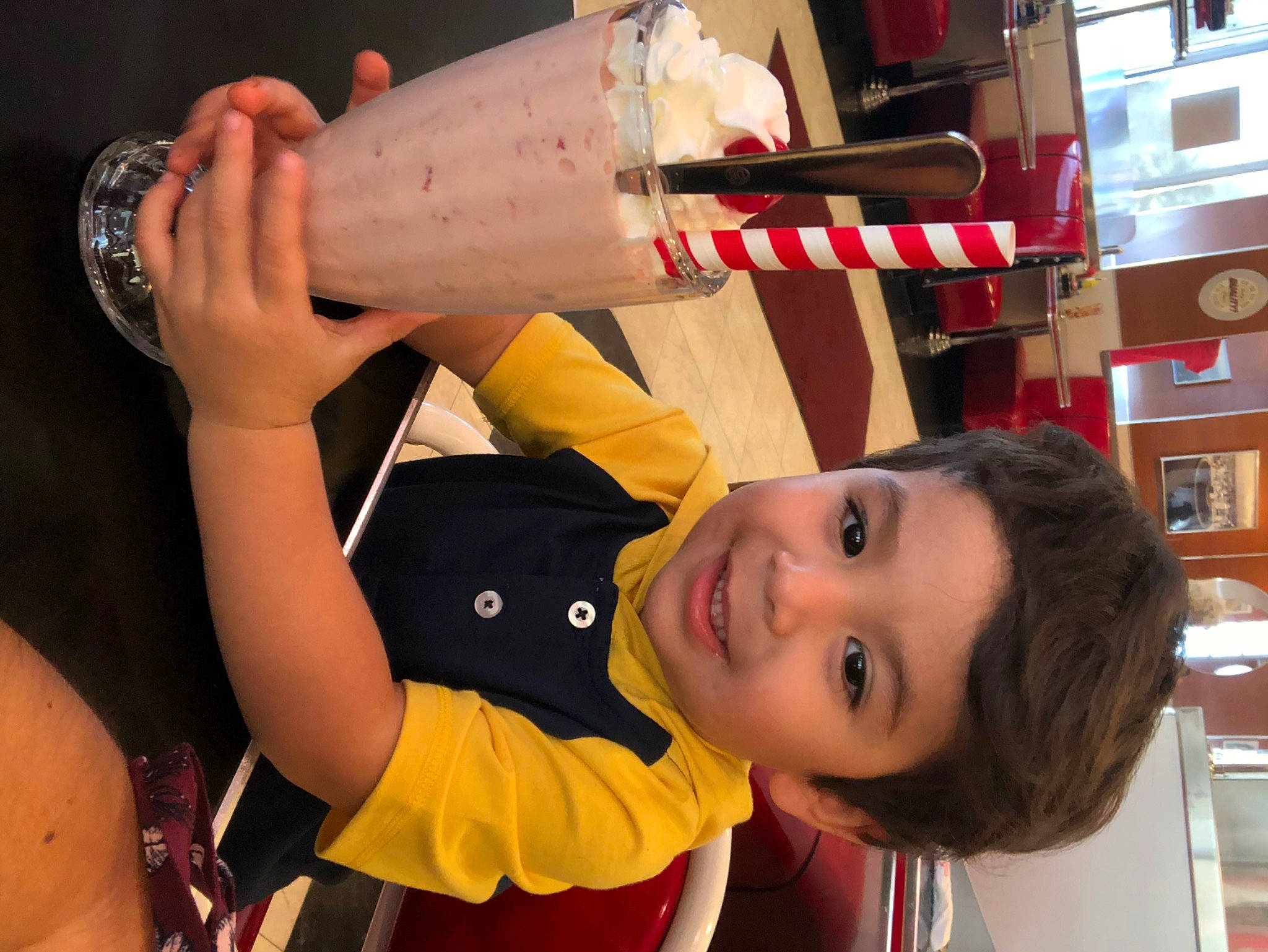 Damian is registered to the contest to win money with this photo: arm, bookcase, child, drink, elbow, event, fun, hand, happy, human_leg, joy, knee, leisure, nail, person, shelf, shelving, smile, t_shirt, thigh