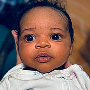 Kenza is registered to the contest to win money with this photo: baby, infant, face, closeup, curious, wide_eyes, expression, clothing, onesie, soft_lighting, portrait, cute, child, newborn, person, skin, head, hand, indoor, focus