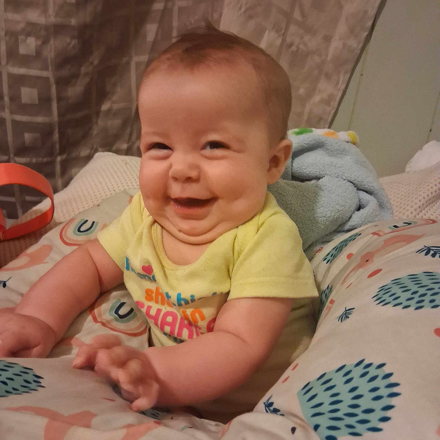 Alita is registered to the contest to win money with this photo: baby, blanket, child, chubby, clothing, cozy, curtain, cute, cute_expression, face, hand, happy, home, indoors, infant, patterned, pillow, portrait, sitting, smile