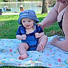 Dennis is registered to the contest to win money with this photo: baby, child, woman, smiling, outdoor, grass, blanket, hat, blue_clothing, park, pond, tree, sunny_day, nature, person, happy, sitting, adult, support, recreation