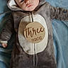 baby, infant, onesie, costume, koala, blanket, blue, wooden_sign, text, lying_down, cute, child, face, hand, foot, soft_texture, milestone, portrait, indoors, clothing