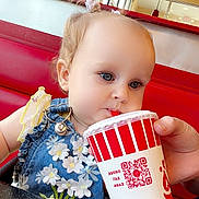 Adalynn is registered to the contest to win money with this photo: toddler, child, drinking, cup, fast_food, restaurant, booth, red_seat, blue_dress, flowers, hair_bows, hand, table, poster, burger, window, light, interior, person, casual