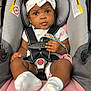 baby, infant, car_seat, headband, clothing, socks, pacifier, black_hair, straps, sitting, pink, gray, child, cute, indoors, closeup, face, hand, toy, secure