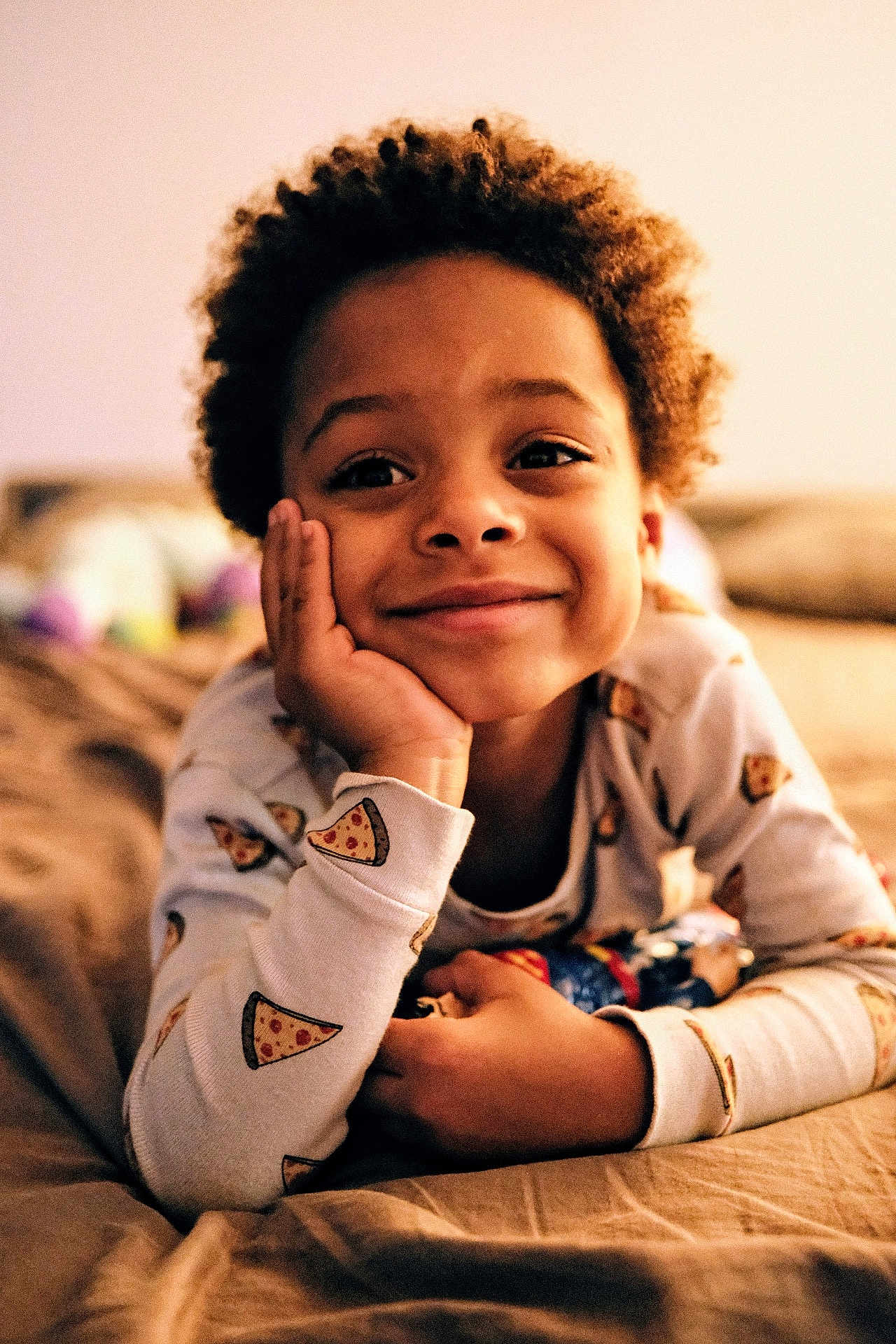 Nils participe au concours pour gagner de l'argent avec cette photo : child, smiling, pajamas, pizza_pattern, curly_hair, bed, cozy, indoor, portrait, relaxed, hand_on_face, casual, young, happy, cute, warm_lighting, home, person, sleepwear, resting