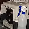 cat, black_cat, pet_carrier, blanket, spray_bottle, blue_nozzle, indoor, dark, shadow, pet, animal, container, plastic, object, floor, household, cozy, peek, hidden, corner