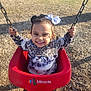 toddler, child, swing, playground, smiling, happy, outdoor, sunlight, curly_hair, bow, red_swing, holding_chains, wood_chips, casual_clothing, cute, joyful, daytime, park, person, fun