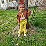 Taylynn is registered to the contest to win money with this photo: child, toddler, tree, grass, flower, sunflower, yellow_pants, orange_bow, outdoor, house, sidewalk, spring, greenery, person, young_child, smiling, portrait, nature, casual_clothing, daylight