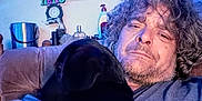 Roxie is registered to the contest to win money with this photo: animal, beard, bottle, brown_hair, casual_clothing, closeup, container, couch, cuddling, curly_hair, dog, furniture, home, indoor, living_room, man, pet, portrait, relaxed, wall_art