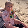 barefoot, beach, blanket, cereal, child, cute, daylight, drinking, juice_box, ocean, outdoor, person, pink_clothing, relaxing, sand, sitting, sunny, toddler, water, waves