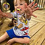 Anthony is registered to the contest to win money with this photo: toddler, child, happy, smiling, bubbles, reaching, sitting, wooden_floor, cartoon_shirt, blue_shorts, playful, joyful, cute, indoor, person, short_hair, barefoot, fun, colorful, closeup