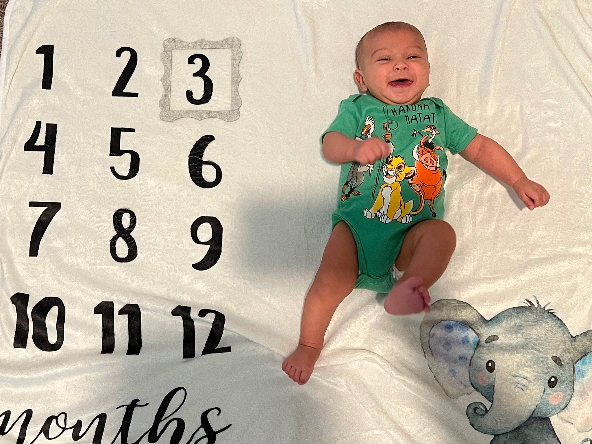 Kai is registered to the contest to win money with this photo: baby, baby_toddler_clothing, child, comfort, design, face, facial_expression, font, happy, linens, pattern, person, play, room, sitting, sleeve, t_shirt, textile, toddler, toy