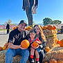 Juliet is registered to the contest to win money with this photo: family, child, pumpkin, pumpkin_patch, hay_bale, outdoor, smiling, man, woman, casual_clothing, fall, seasonal, nature, blue_sky, sunlight, hat, socks, footwear, people, portrait