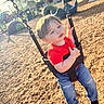toddler, child, swing, playground, red_shirt, blue_jeans, sunlight, outdoor, daylight, wood_chips, play_equipment, chain, smiling, casual_clothing, black_shoes, young_child, recreation, fun, park, leisure