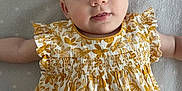 Alma participe au concours pour gagner de l'argent avec cette photo : arms, baby, baby_clothes, blanket, child, closeup, cute, dress, eyes, face, floral_pattern, human, indoors, infant, lying_down, portrait, smile, soft_texture, yellow, young_child