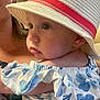 baby, child, hat, white_hat, red_band, blue_dress, floral_pattern, portrait, indoor, person, face, skin, eyes, shoulder, clothing, holding, adult, closeup, cute, infant