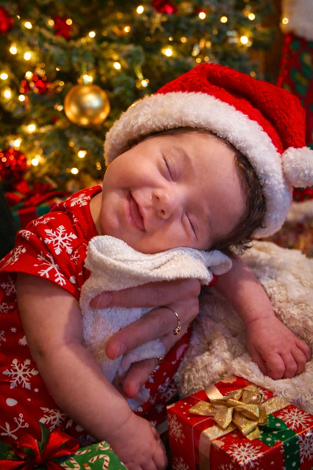 Gwen is registered to the contest to win money with this photo: baby, infant, smiling, santa_hat, christmas_tree, christmas_lights, holiday, presents, gift_box, red_clothing, snowflake_pattern, towel, happy, festive, holiday_season, cute, warm, cozy, celebration, portrait