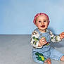 baby, infant, toddler, child, smiling, blue_background, denim_overalls, bandana, red_bandana, patterned_shirt, dinosaur_print, sitting, barefoot, studio_floor, portrait, happy, reaching, bright_eyes, headscarf, cute