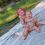 Rosalyn is registered to the contest to win money with this photo: child, baby, toddler, smiling, happy, pink_hair, outdoor, backyard, grass, portrait, sitting, lying_down, infant, siblings, playful, blanket, sheet, sunlight, wheelie_bin, family