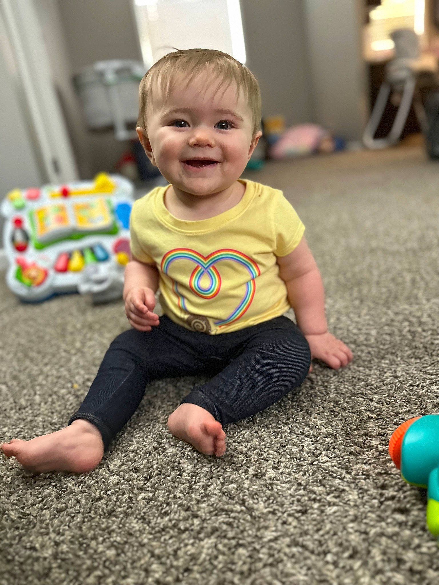 Violette is registered to the contest to win money with this photo: baby, baby_playing_with_toys, baby_toddler_clothing, child, event, floor, flooring, fun, happy, joy, pattern, person, play, room, sitting, skin, sleeve, smile, standing, t_shirt