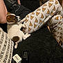 puppy, dog, pet, couch, black_fabric, person, pajama_pants, cartoon_print, deer_faces, relaxed, indoor, home, cozy, animal, small_dog, white_dog, brown_spots, resting, casual, curious