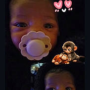Paris is registered to the contest to win money with this photo: baby, pacifier, infant, face, closeup, blanket, cute, child, portrait, dark_background, expression, eyes, cartoon_monkeys, text_overlay, love, adorable, newborn, sleepwear, head, cozy
