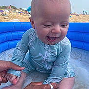 Soan participe au concours pour gagner de l'argent avec cette photo : baby, infant, child, swimsuit, inflatable_pool, beach, sand, water, happy, smiling, sitting, adult_hands, summer, vacation, outdoor, sunny, playful, closeup, blue, fun