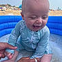 baby, infant, child, swimsuit, inflatable_pool, beach, sand, water, happy, smiling, sitting, adult_hands, summer, vacation, outdoor, sunny, playful, closeup, blue, fun
