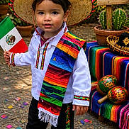 Leo is registered to the contest to win money with this photo: child, boy, sombrero, mexican_flag, traditional_clothing, serape, confetti, outdoor, celebration, cinco_de_mayo, colorful, maracas, cactus, sign, festive, smiling, street, party, holiday, decorations