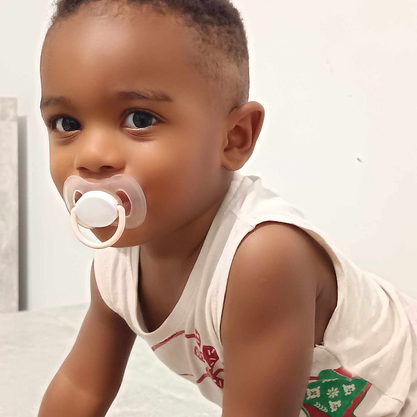 Bachir a rejoint le concours — aidez-le/la à gagner de superbes lots ! arm, baby, brown_skin, casual_clothing, child, closeup, curious, cute, expression, face, indoor, infant, looking, pacifier, portrait, short_hair, sleeveless_shirt, toddler, white_background, young_child