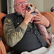 Wiggles is registered to the contest to win money with this photo: affection, black_shirt, blanket, brown_fur, camouflage, casual_clothing, comfort, couch, dog, facial_hair, glasses, hand, home, indoor, man, pet, relaxed, seated, tongue_out, watch