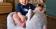Jonah is registered to the contest to win money with this photo: baby, bare_feet, blue_shirt, child, cozy, elephant, furniture, happy, home, indoor, infant, living_room, photography, plush_toy, portrait, rocking_toy, sitting, smiling, toy, wooden_floor