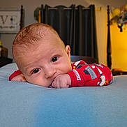 Jonah is registered to the contest to win money with this photo: baby, child, infant, lying_down, blanket, red_clothing, hand, face, eyes, indoors, bedroom, curtains, soft_texture, cute, portrait, sleepwear, warm_lighting, cozy, young_child, closeup