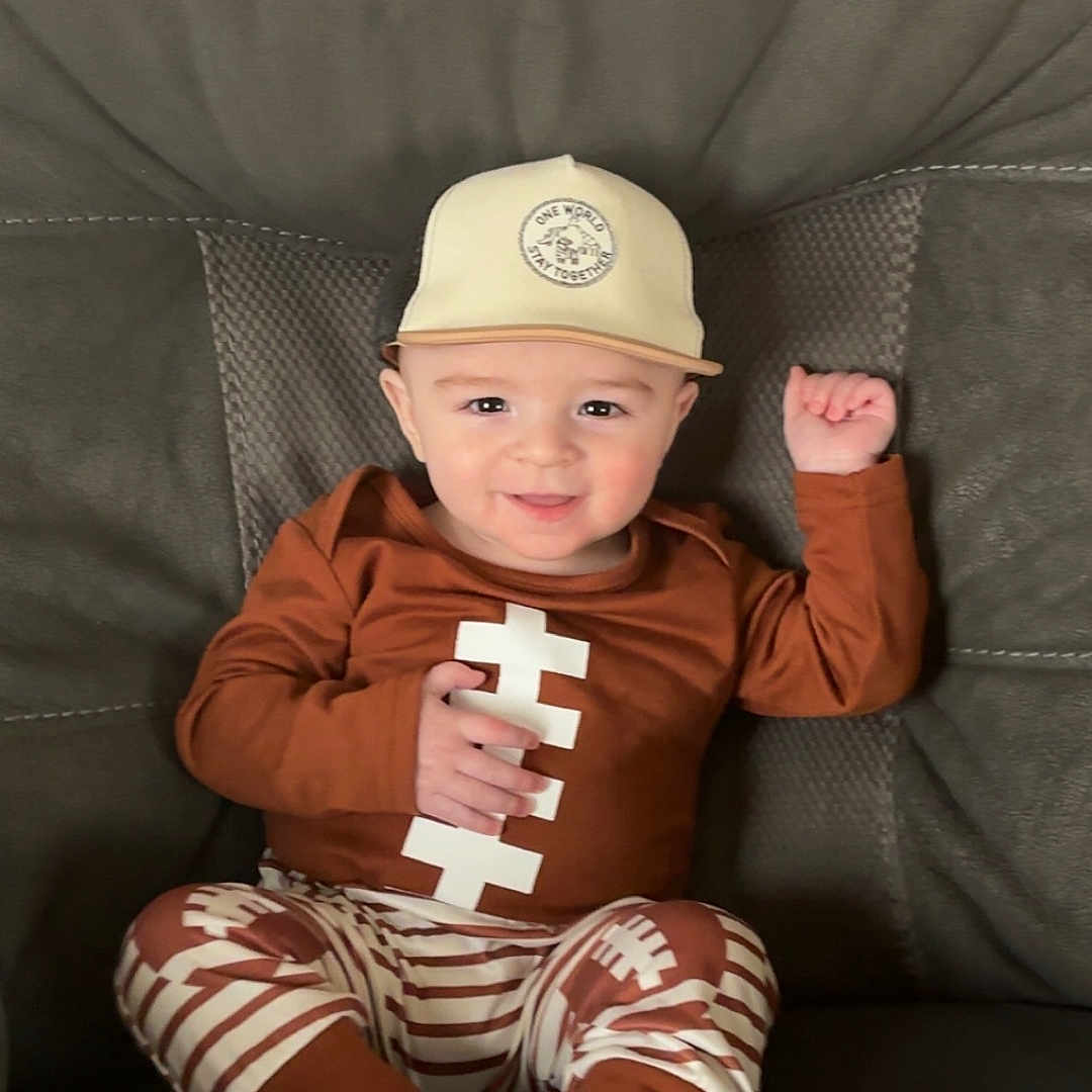 Kreedon joined the competition — help win amazing prizes! baby, brown_clothing, casual, child, couch, cozy, cute, face, football_theme, happy, hat, indoor, person, portrait, raised_hand, sitting, smiling, socks, striped_pants, young_child
