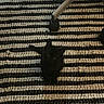 black_cat, kitten, striped_rug, indoor, floor, office_chair, wheel, pet, animal, small, curious, looking_up, texture, pattern, black, white, cozy, home, furniture, domestic