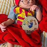 Jiren is registered to the contest to win money with this photo: baby, child, cozy, cute, feet, glasses, hand, harry_potter, hat, indoors, infant, milestone_sign, onesie, portrait, red_blanket, resting, sleeping, soft_lighting, striped_bed_sheet, winnie_the_pooh