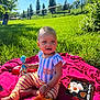 child, toddler, toy, blanket, grass, outdoor, sunny, park, greenery, person, playtime, colorful, clothing, baby, nature, daylight, smiling, sitting, cute, recreation