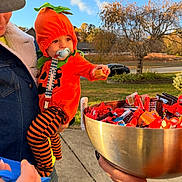 Lawson joined the competition — help win amazing prizes! toddler, child, pumpkin_costume, candy, bowl, adult, denim_jacket, pacifier, outdoor, sidewalk, tree, car, costume, autumn, orange, striped_pants, hand, sky, grass, holiday
