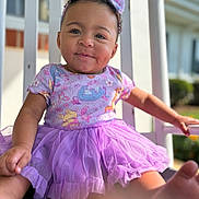 Ryver joined the competition — help win amazing prizes! baby, child, infant, portrait, smiling, happy, outdoor, porch, purple_dress, tutu, bow, curly_hair, sitting, dress, floral_pattern, barefoot, sunlight, railing, closeup, cute