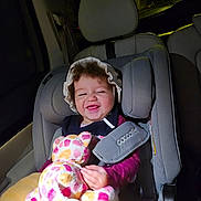 Sara participe au concours pour gagner de l'argent avec cette photo : toddler, child, car_seat, stuffed_animal, blanket, bonnet, smiling, happy, indoors, seat_belt, car_interior, night, curly_hair, clothing, person, toy, safety, seat, baby, cute
