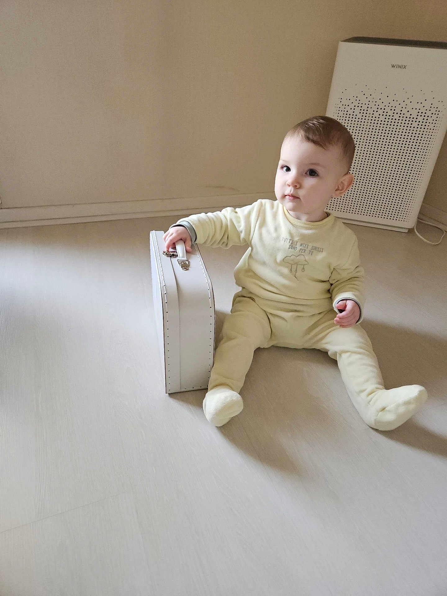 Sasha participe au concours pour gagner de l'argent avec cette photo : baby, child, sitting, yellow_pajamas, suitcase, floor, indoor, air_purifier, minimalist, light, cozy, curious, childhood, person, furniture, modern, home, expression, young, casual