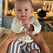 Léon participe au concours pour gagner de l'argent avec cette photo : baby, child, hands, person, infant, smile, face, clothing, striped_pants, long_sleeve_shirt, wooden_surface, kitchen, blurred_background, indoor, portrait, cute, young_child, skin, happy, closeup