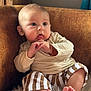 Léon participe au concours pour gagner de l'argent avec cette photo : baby, child, infant, face, hands, feet, striped_pants, beige_top, fluffy_rug, brown_couch, wood_background, curious_expression, indoors, soft_lighting, portrait, sitting, cute, young, skin, person
