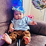 baby, party_hat, birthday, couch, donut, chocolate, candles, balloon, dinosaur, celebration, indoors, child, curious, clothing, blue_shirt, brown_pants, feet, relaxed, festive, home