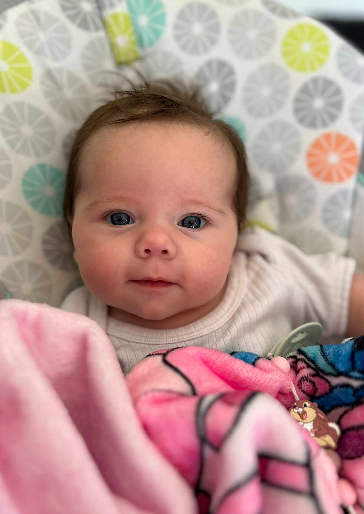 Rose a rejoint le concours — aidez-le/la à gagner de superbes lots ! baby, infant, face, blanket, pink, blue, white_clothing, patterned_background, curious, closeup, child, cute, soft_texture, indoors, pacifier_clip, expression, head, small_hands, toddler, young_child
