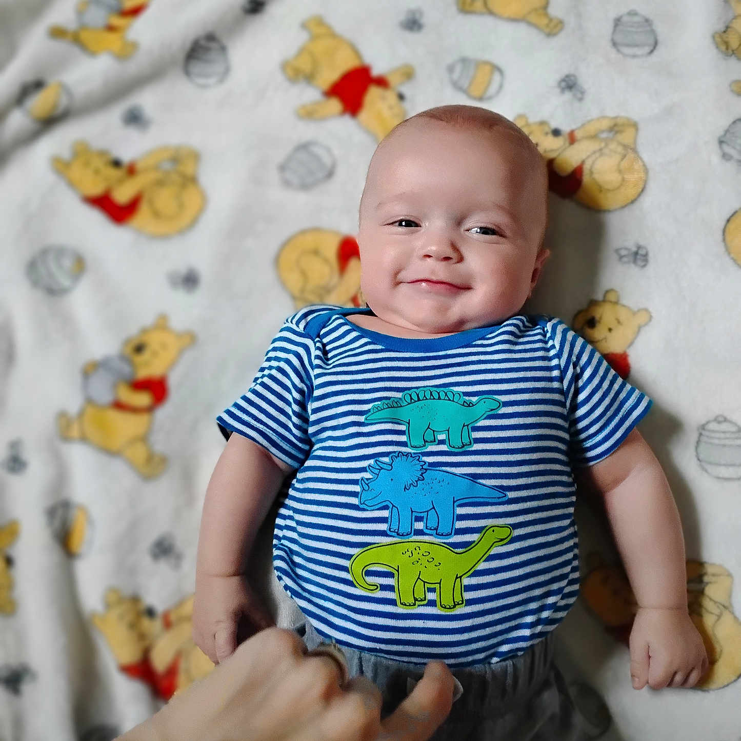 Elieh is registered to the contest to win money with this photo: baby, blanket, cartoon, child, clothing, cute, dinosaur_print, hand, happy, indoors, infant, lying_down, pattern, person, playful, portrait, smile, soft_toys, striped_shirt, winnie_the_pooh