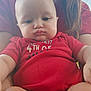 baby, child, person, red_clothing, onesie, face, arms, legs, hair, blue_eyes, skin, expression, sitting, holding, casual, indoor, portrait, young_child, human, closeup